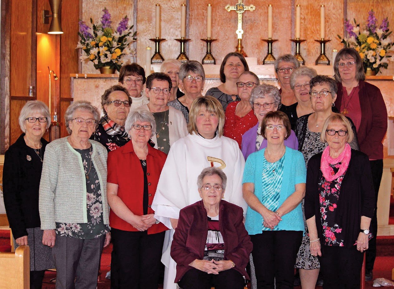 Group of women in a church in front of an altar with flowers and candles.