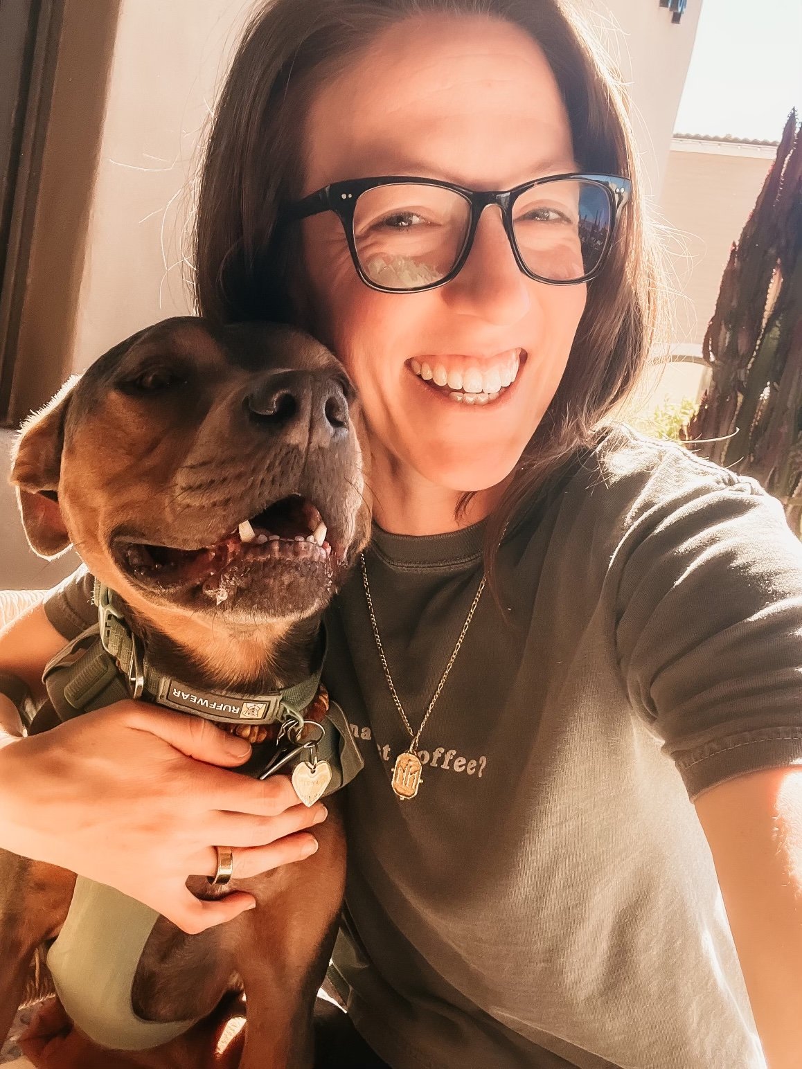 Dr. Elizabeth smiling in warm sunlight while holding her dog Luna, reflecting nervous system safety, co-regulation, and embodied presence at the end of a blog about body-led healing.