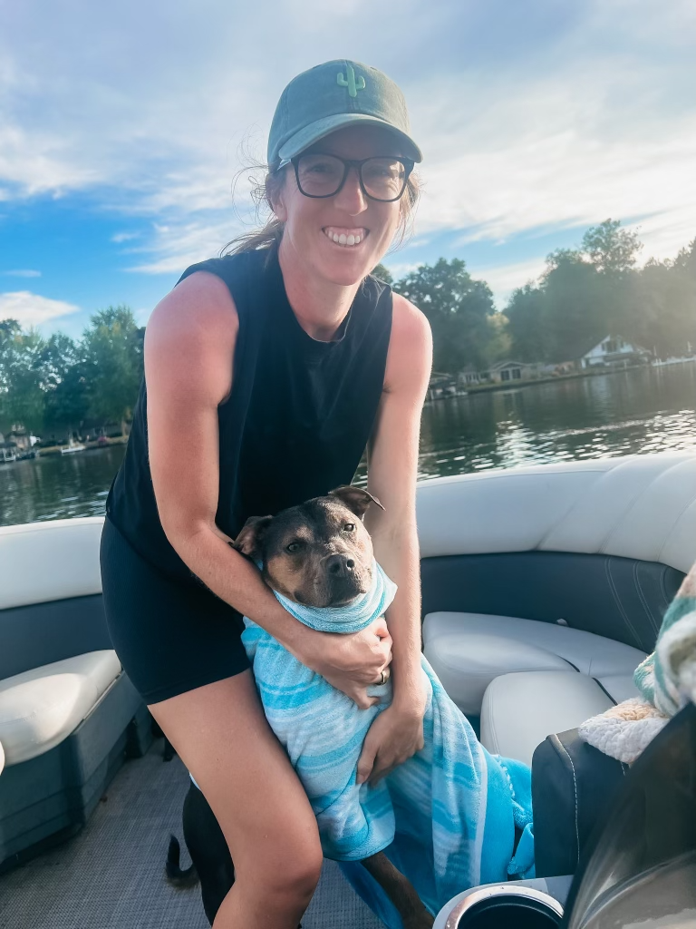 Dr. Elizabeth smiling and hugging her dog on a boat outdoors
