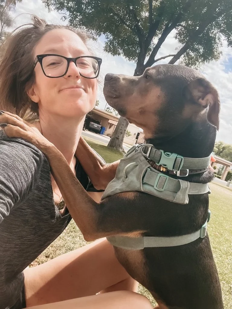 Woman sitting outdoors with her dog placing paws on her shoulders, representing tension, connection, and nervous system awareness