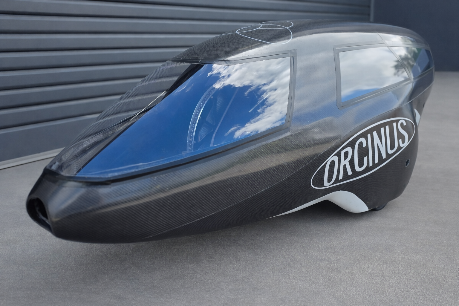 Close-up of a sleek, black carbon fiber racing trike marked with the logo 'ORCINUS' in white lettering.