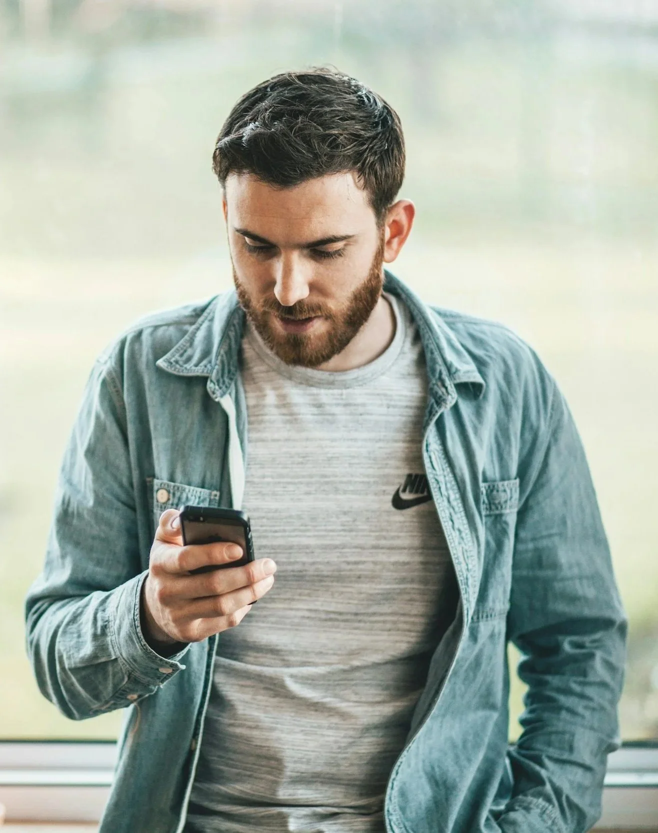 Man with dark hair and a beard wearing a denim shirt holding his phone booking an escort using manners and basic etiquette