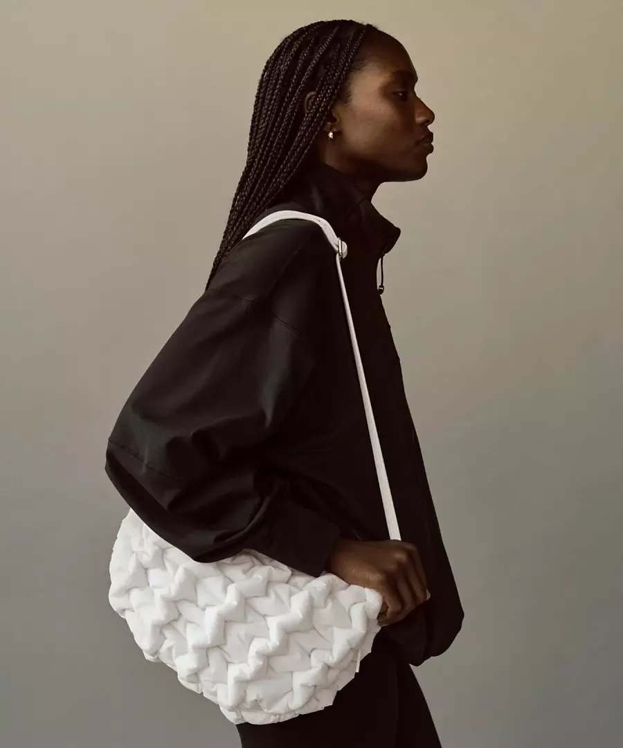 Woman with braided hair wearing a black jacket holding a white textured bag