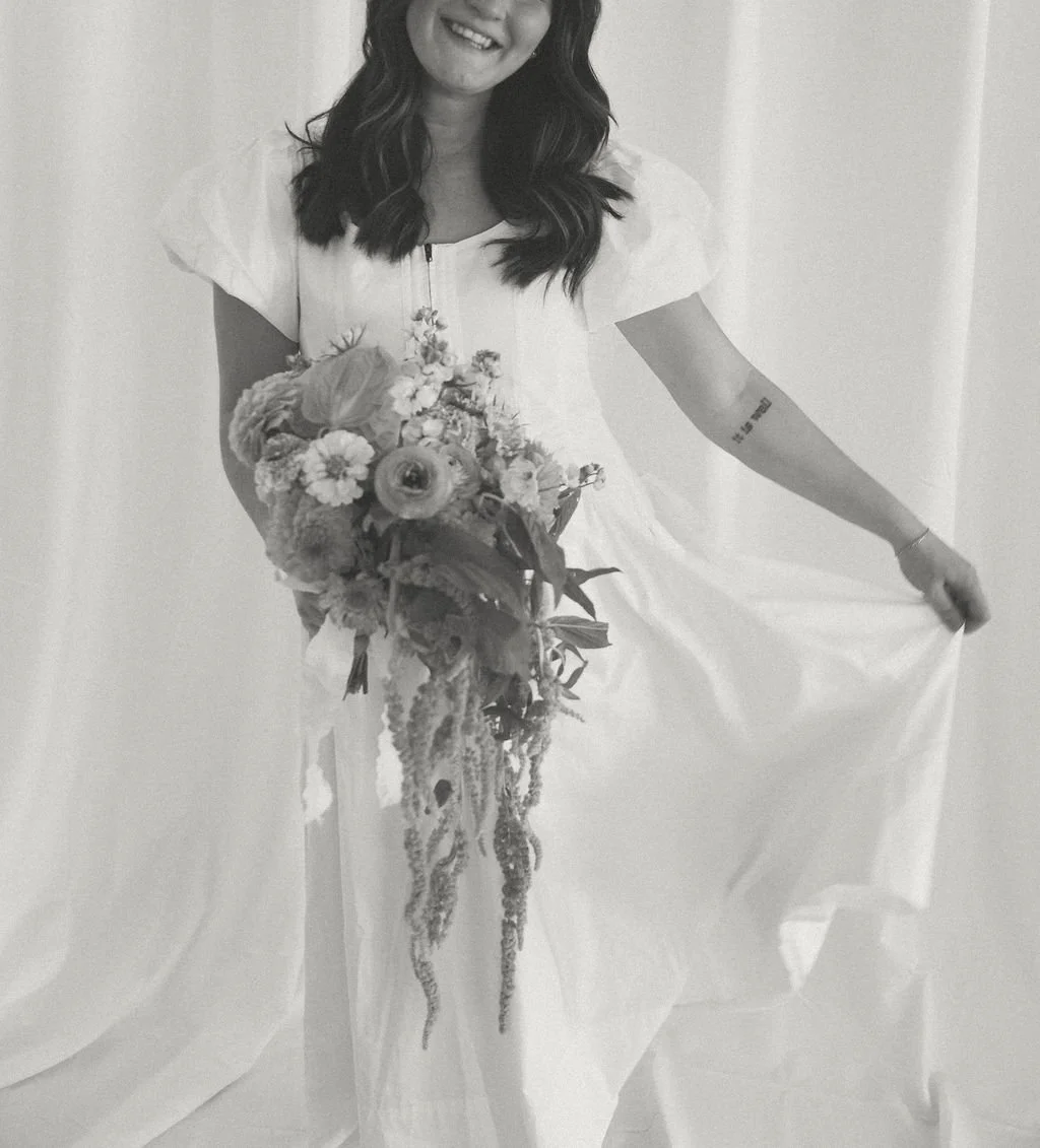 Woman in white dress holding a large floral bouquet, smiling in a monochrome photograph.