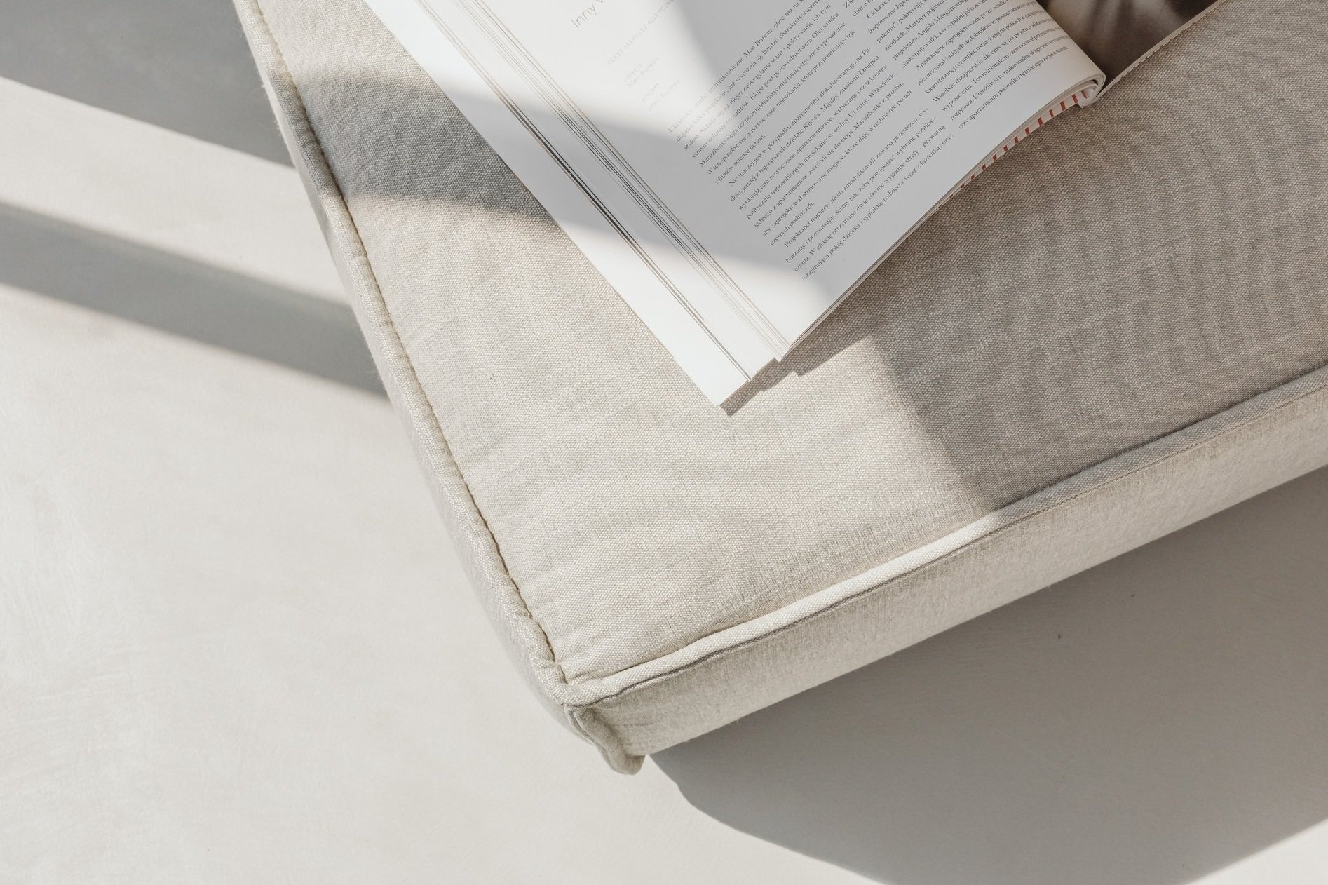 Open magazine on a light beige sofa in sunlight.