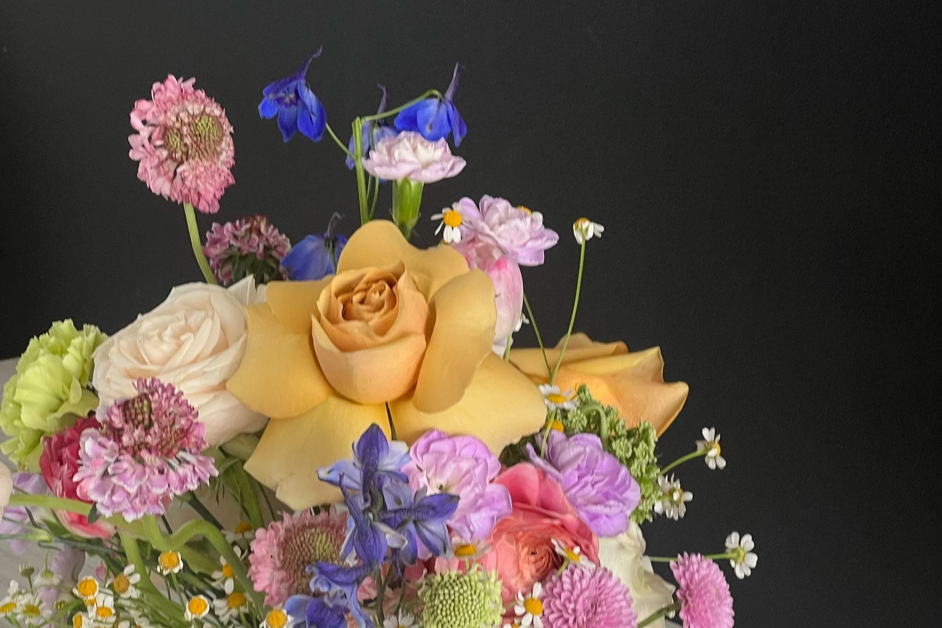 Assorted flower arrangement with roses and wildflowers against dark background.
