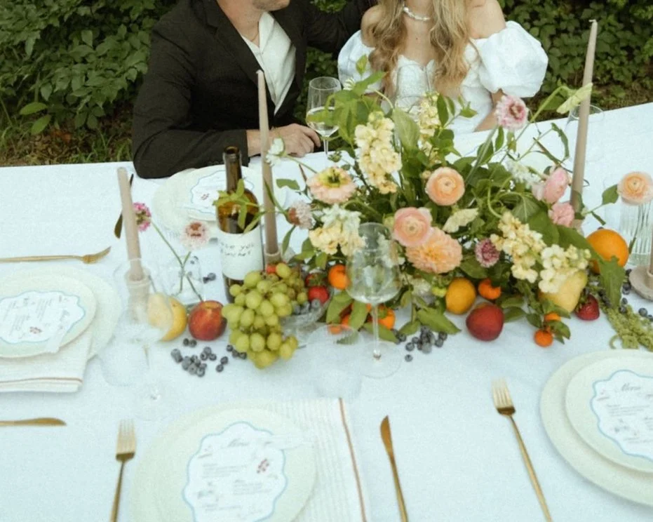 Elegant outdoor dining setup with floral centerpiece, fruits, and tableware.