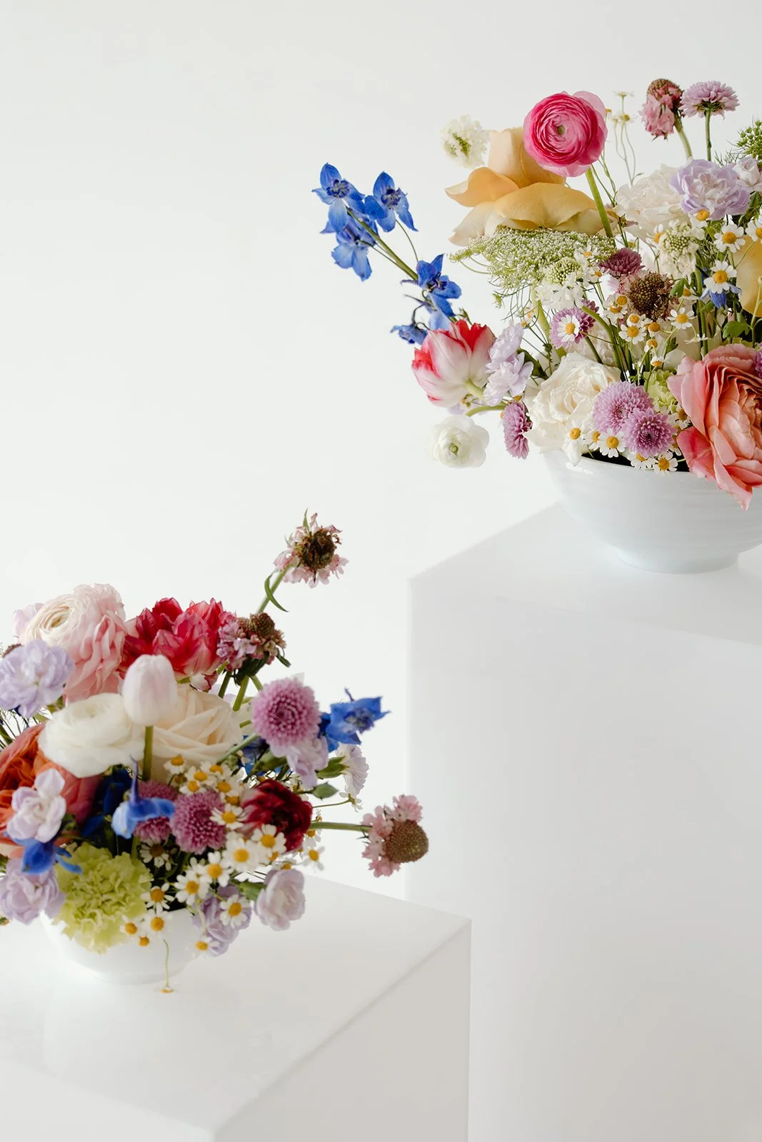 Colorful floral arrangements with various flowers in white bowls on white pedestals.