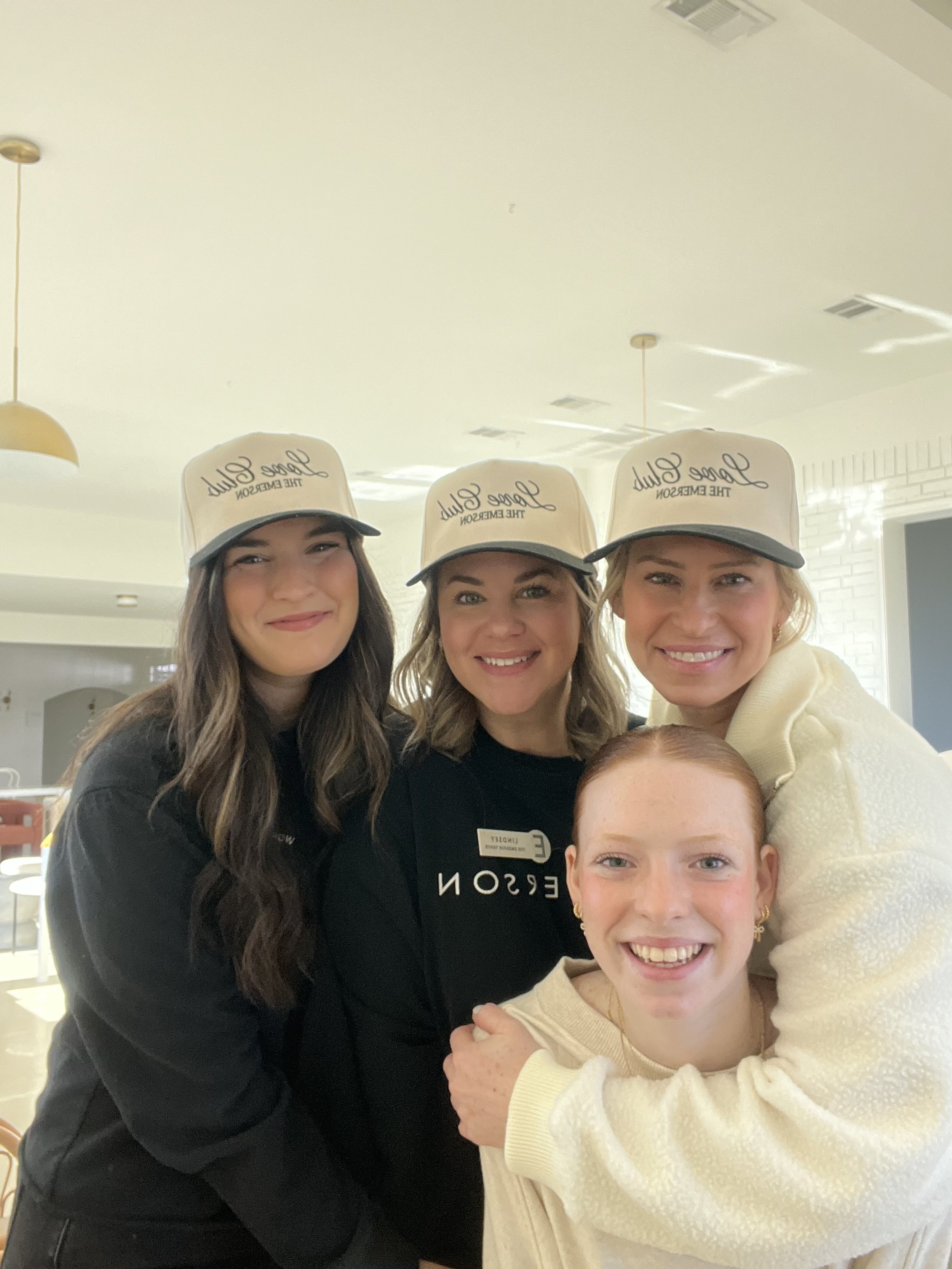 Group of four women smiling, three wearing hats with the text "Love Club The Emerson."