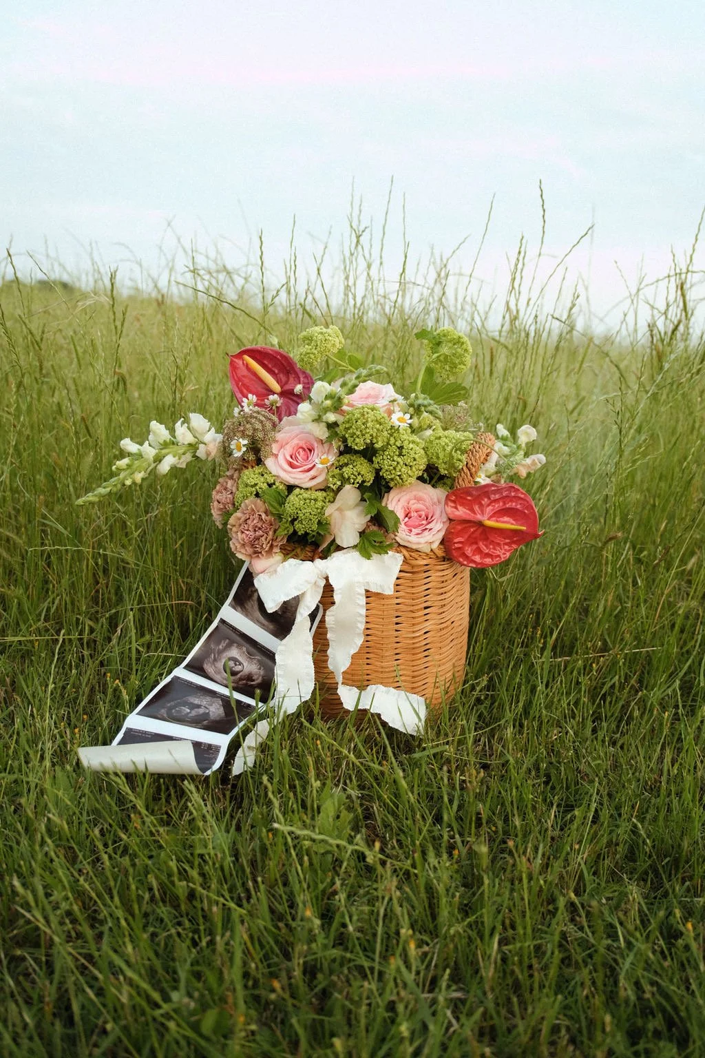 Basket with colorful flowers and ultrasound images in a grassy field.
