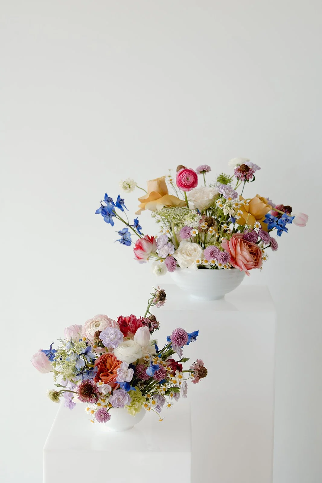 Colorful floral arrangements in white bowls on pedestals