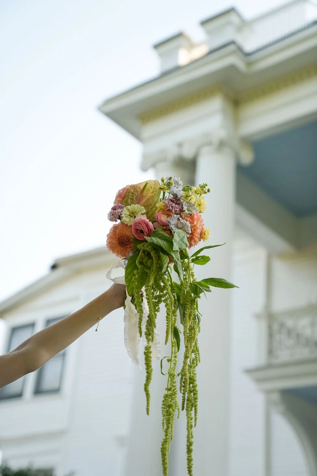 A hand holding a bouquet of colorful flowers with a historic white building in the background.