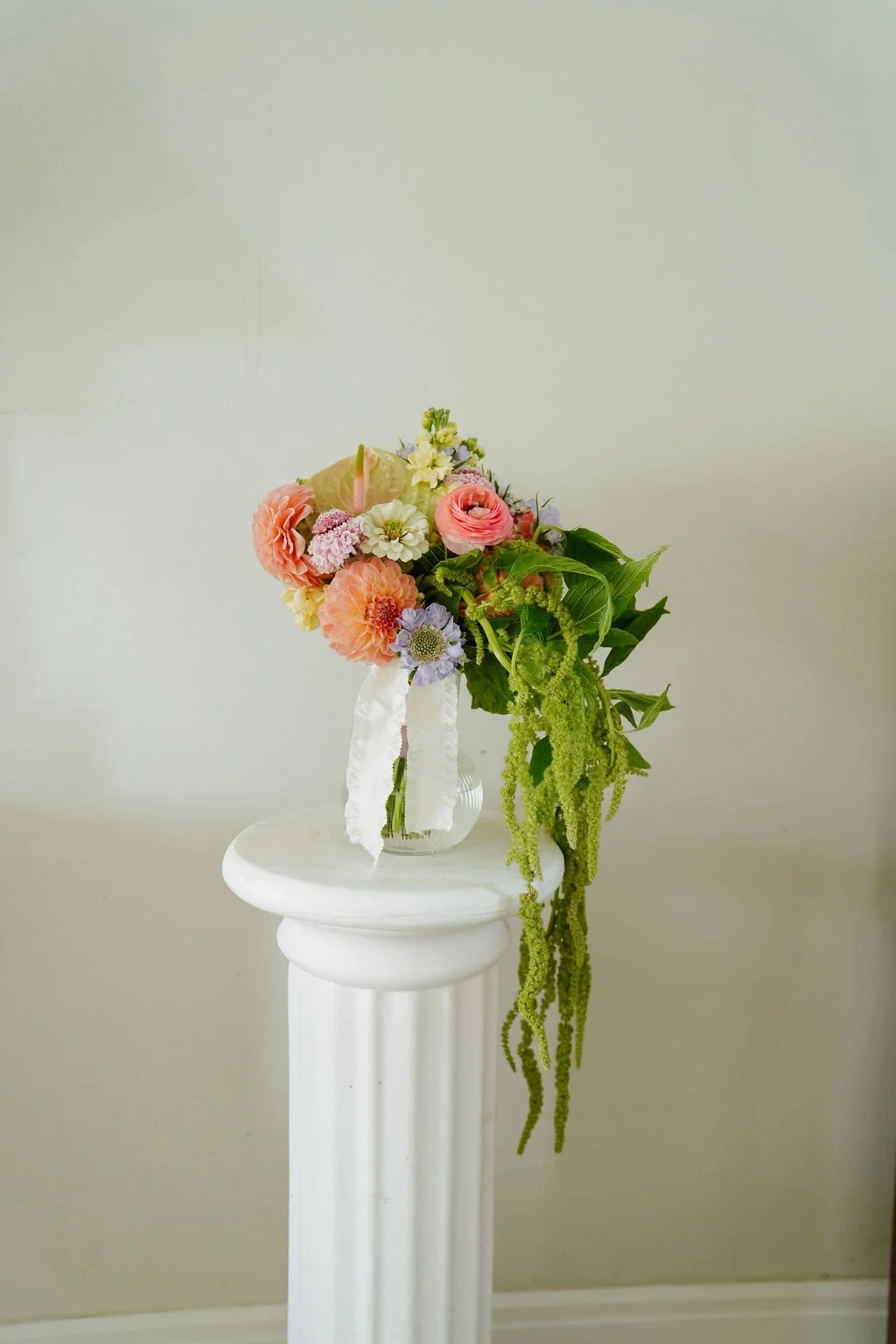 Colorful flower bouquet on white pedestal with green draping foliage.