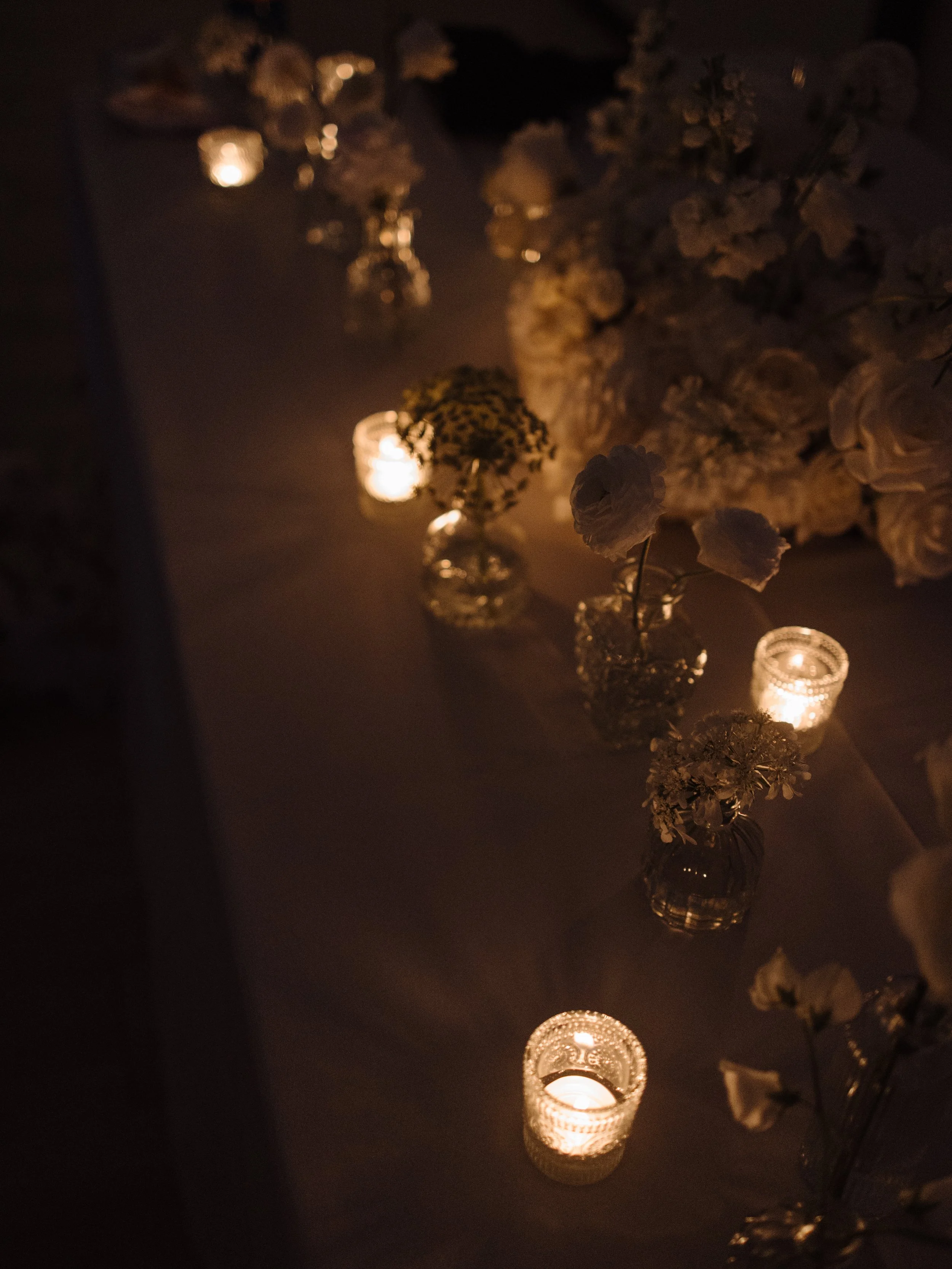 Dimly lit table with candles and white flowers in glass vases