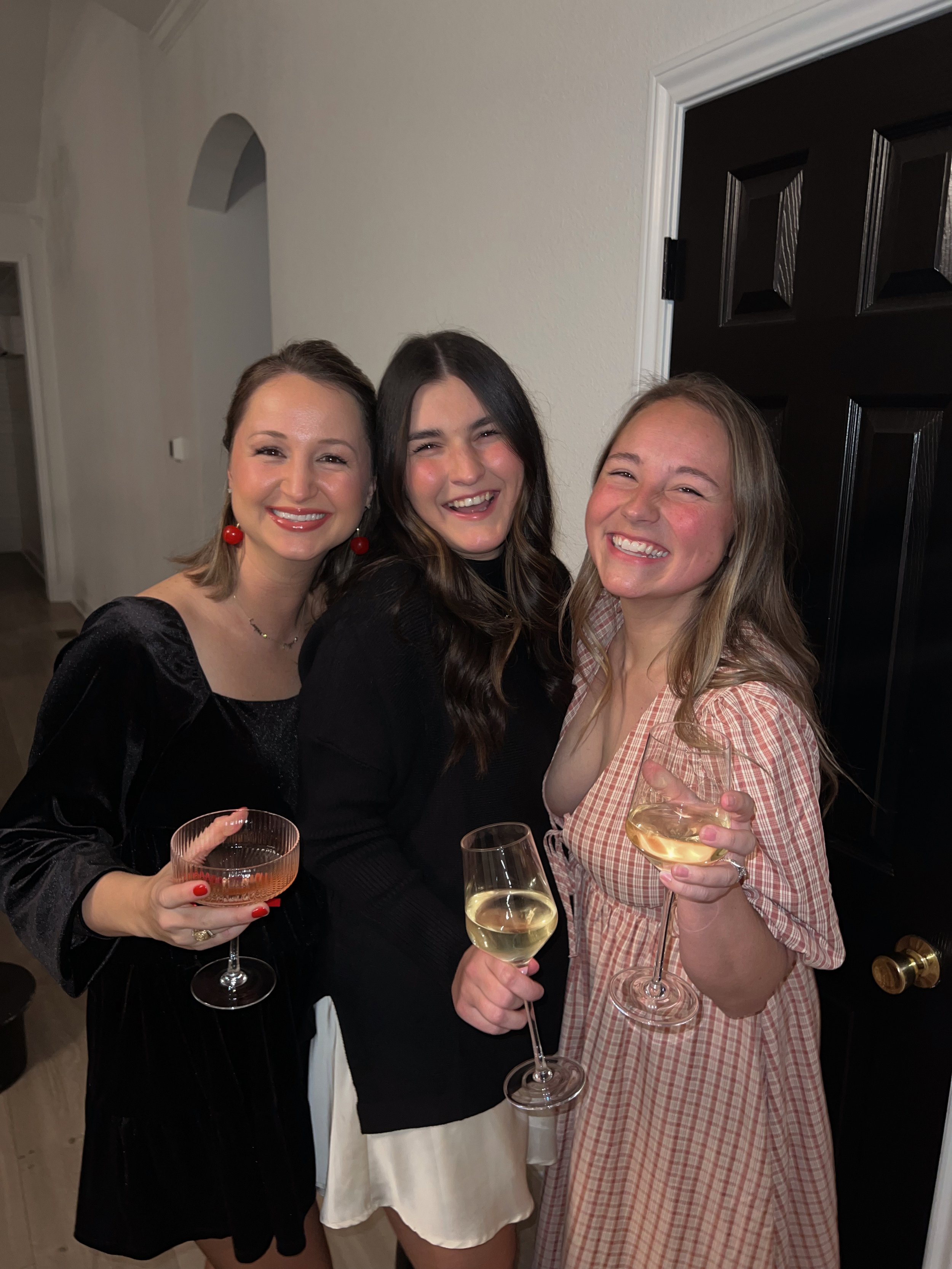 Three women smiling and holding wine glasses in a room with a black door.