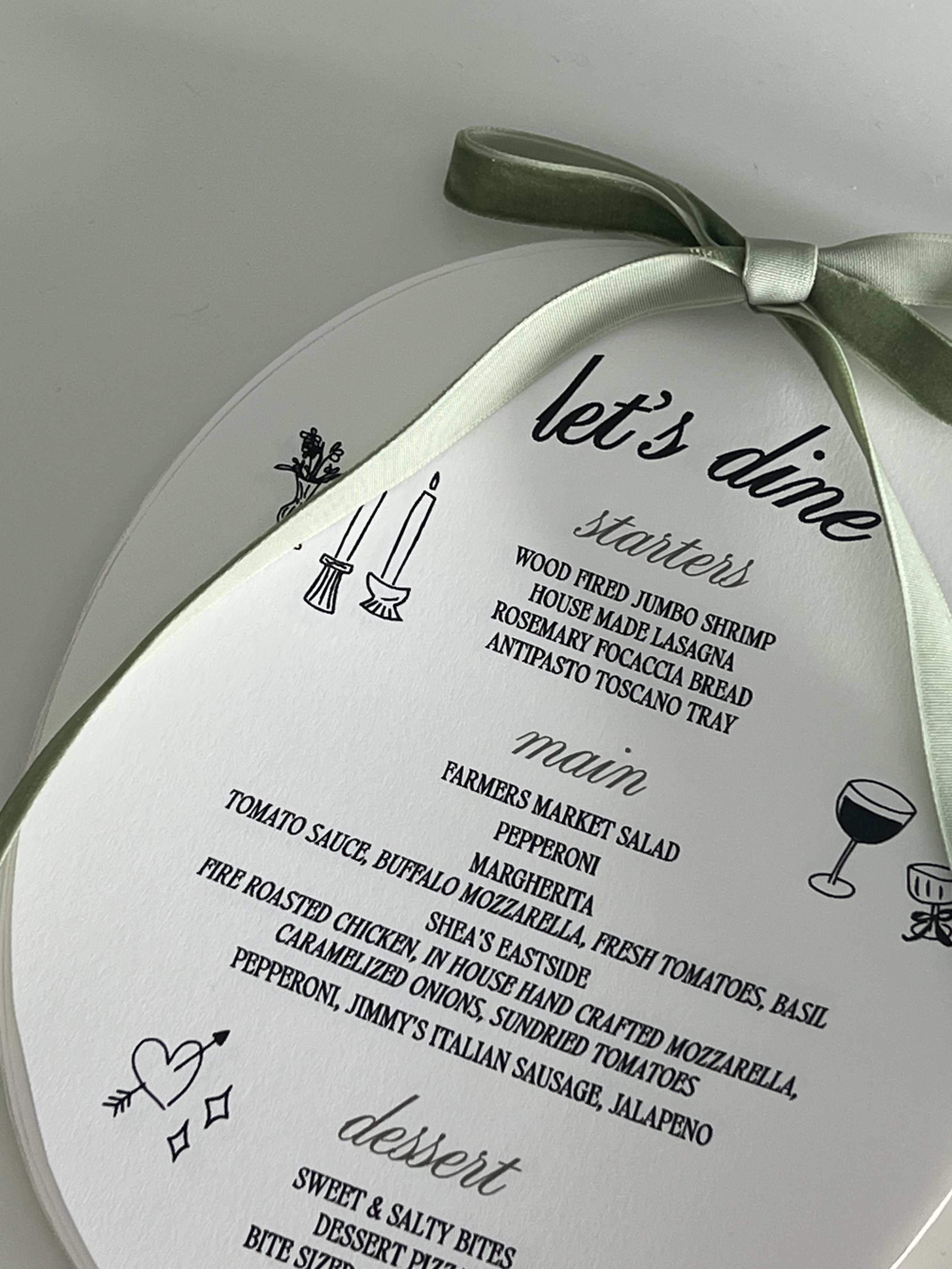 Decorative dining menu with green ribbon, featuring sections for starters, main dishes, and dessert. Includes illustrated candle and wine glass icons.