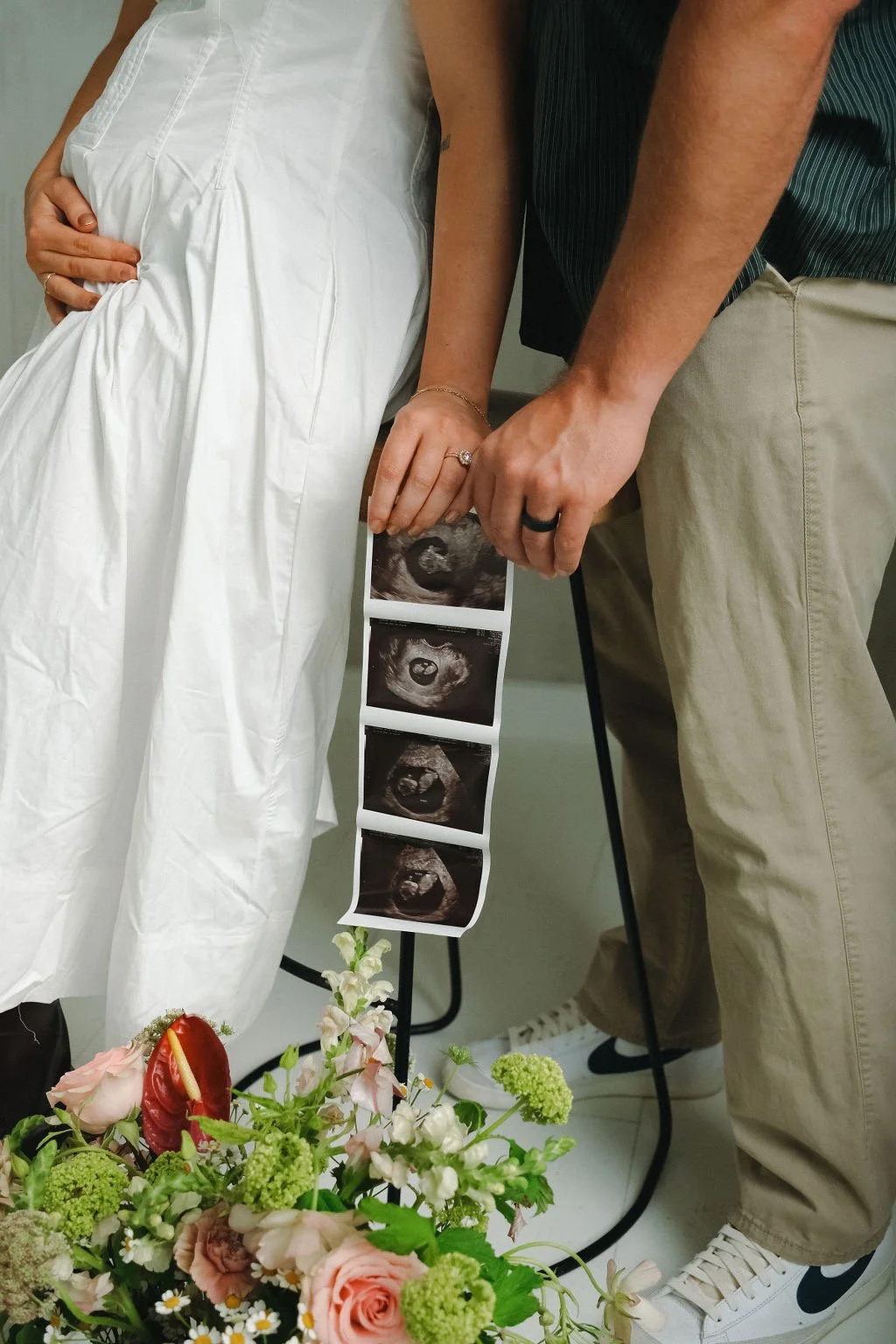 Pregnant couple holding ultrasound pictures with flowers in the foreground.