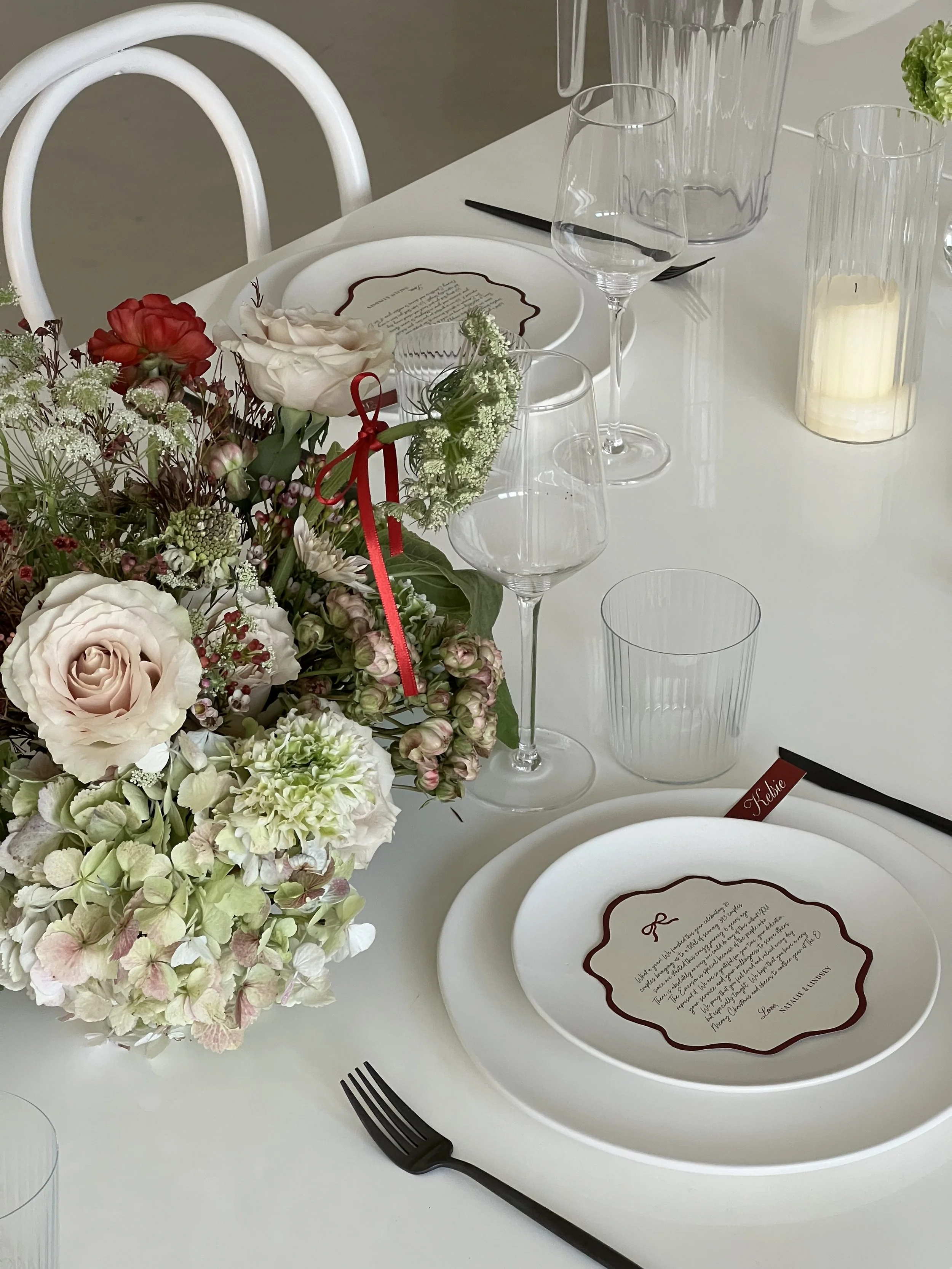 Elegant table setting with white plates, floral centerpiece, wine glasses, and a menu card.