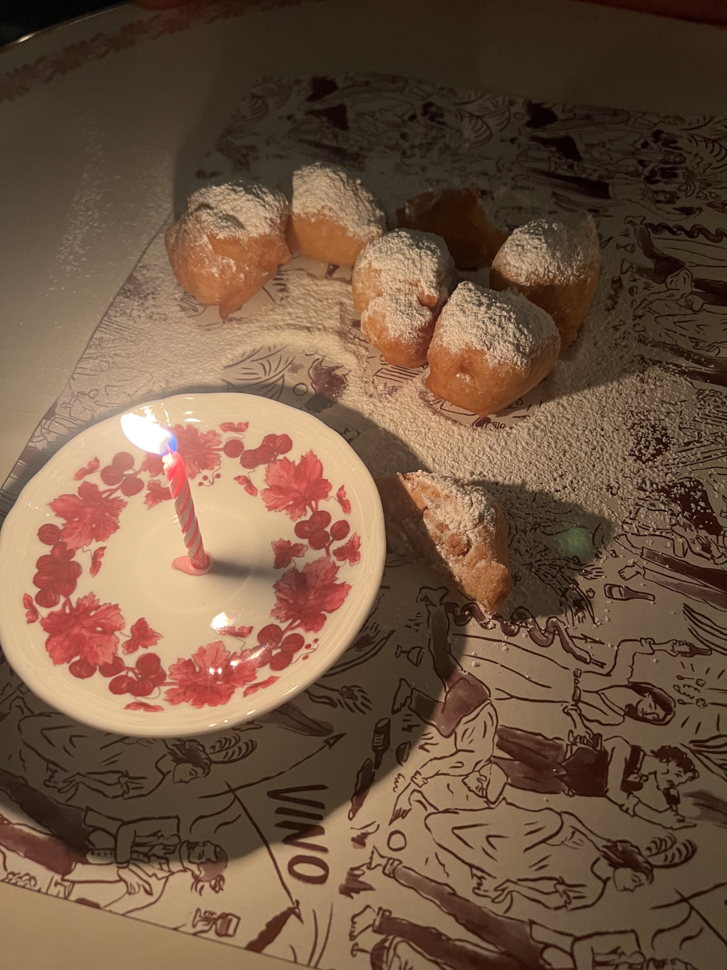 A group of pastries covered in powdered sugar and arranged around a small plate with a lit birthday candle on a decorative table setting.