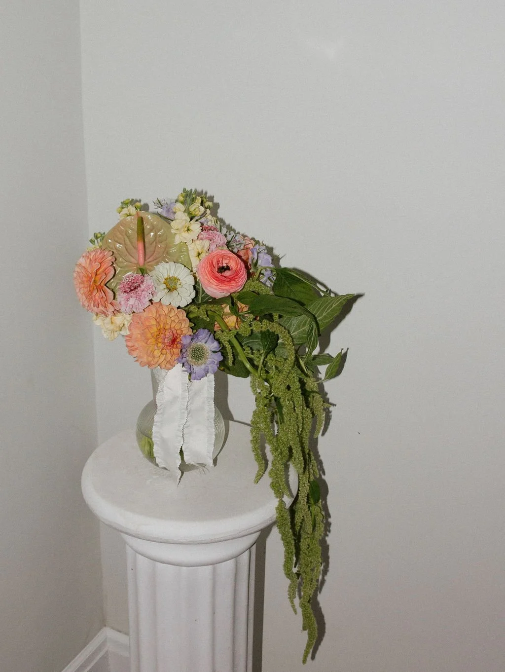 A floral arrangement in a clear vase on a white pedestal, featuring assorted colorful flowers and greenery.
