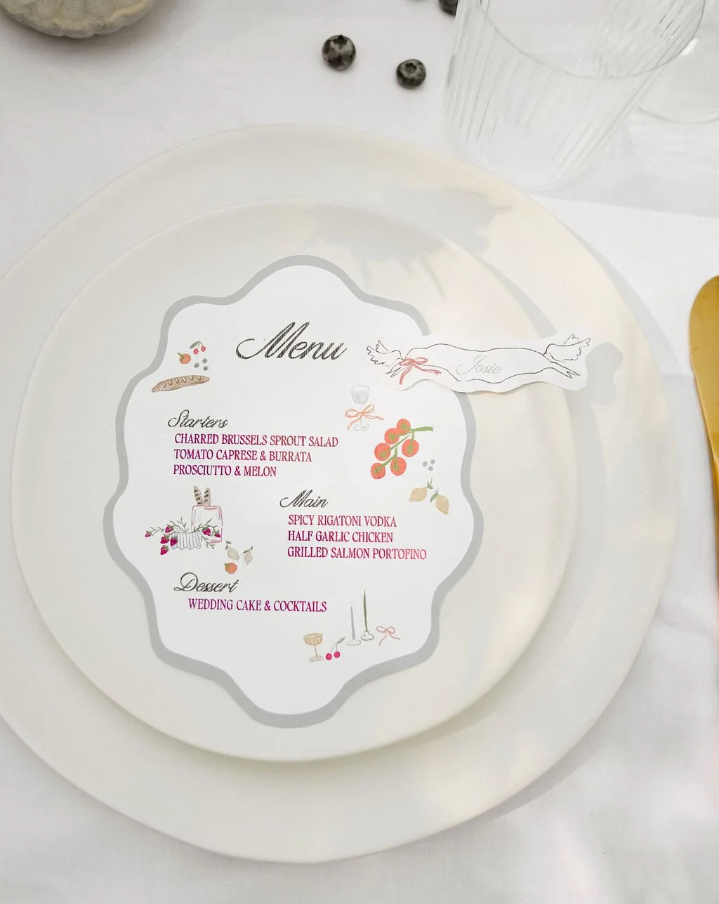 Elegant wedding menu on a dinner plate featuring starters, main courses, and dessert with a decorative name card 'Josie' on a white table setting.