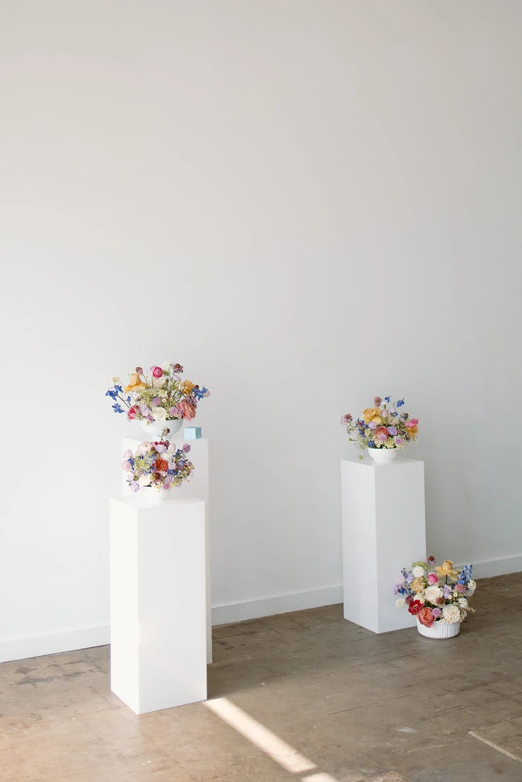Floral arrangements displayed on white pedestals against a plain wall.