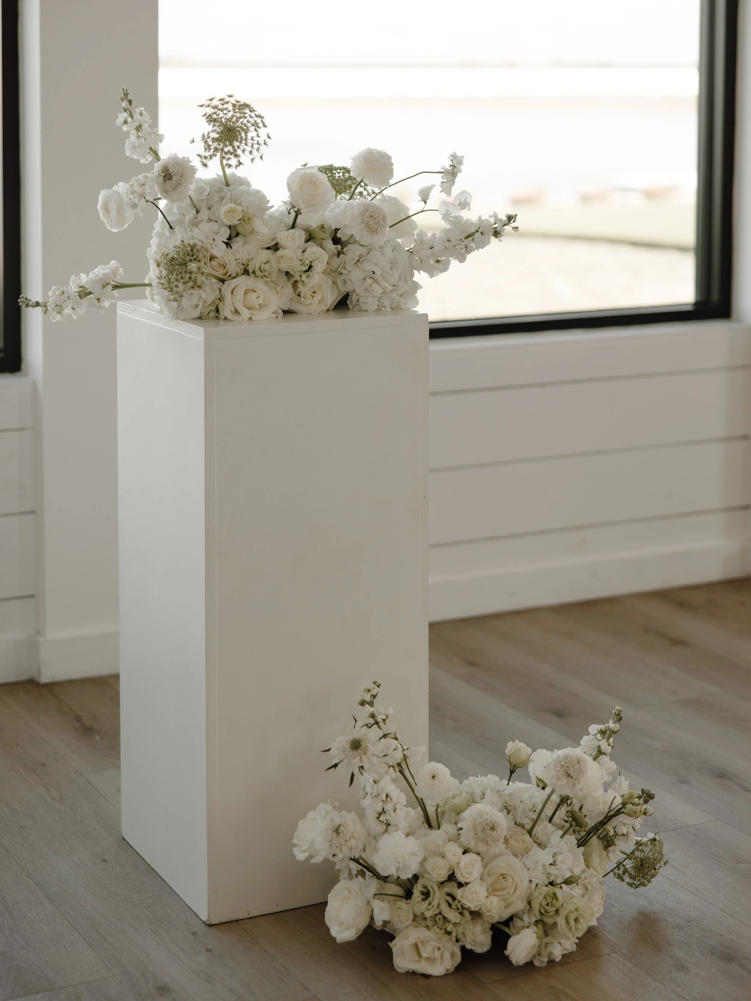 White floral arrangements on a pedestal and floor indoors.