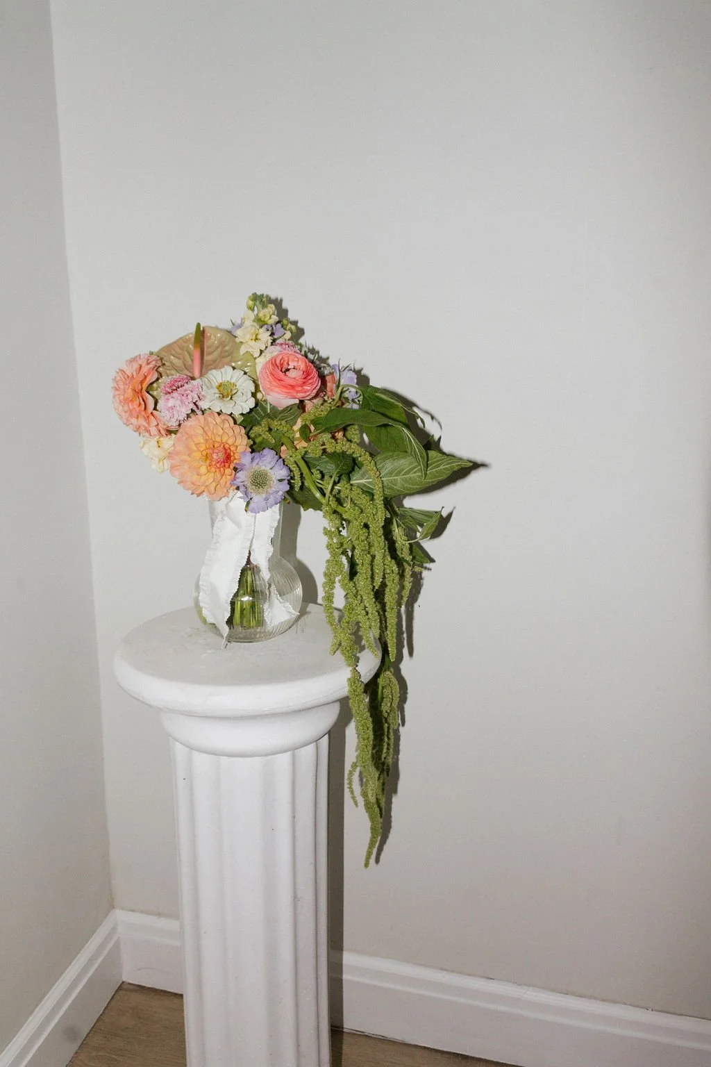 A floral arrangement with pink, peach, and white flowers in a vase on a white pedestal.