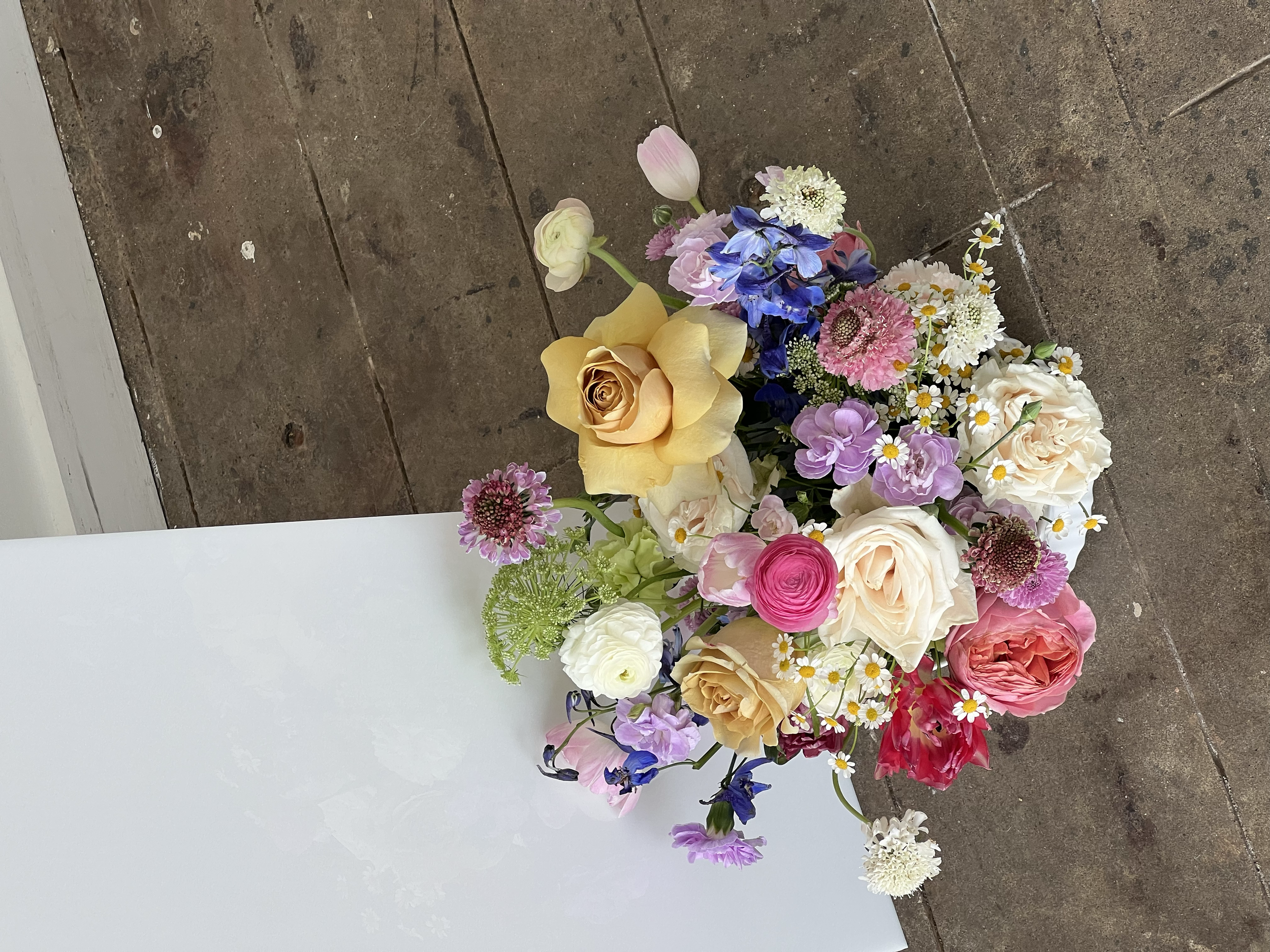 A colorful bouquet of mixed flowers including roses, daisies, and other blooms on a wooden surface.