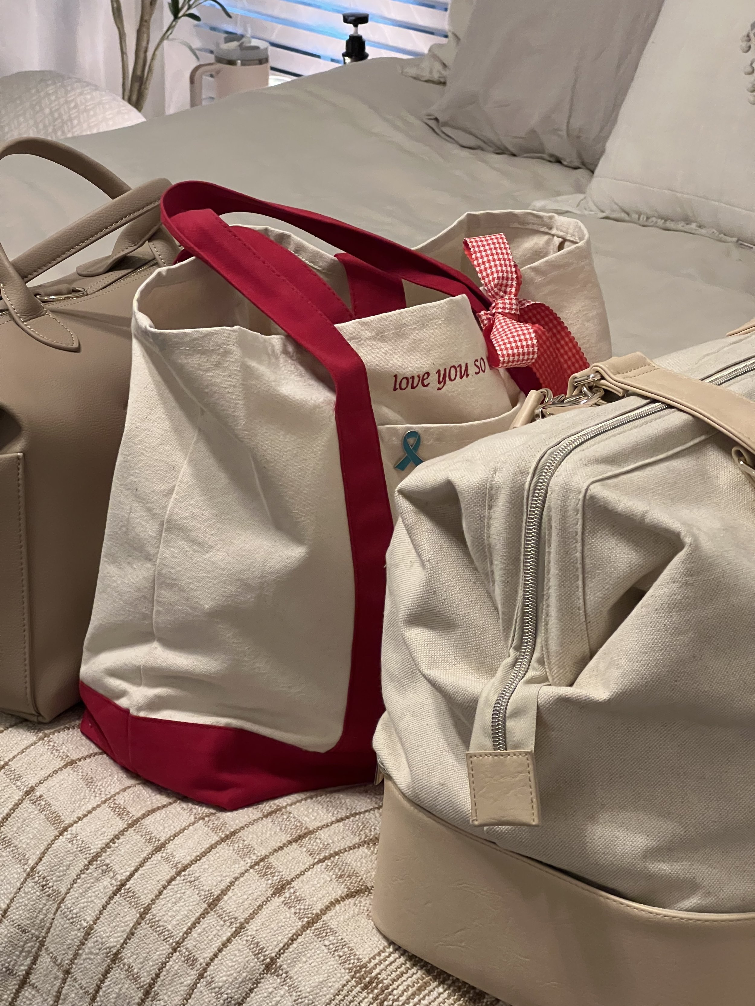 Tote bags and a travel bag on a bed with white bedding.