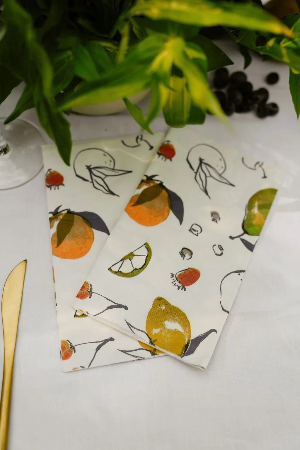 Table setting with citrus-themed napkins, golden cutlery, and leafy plants