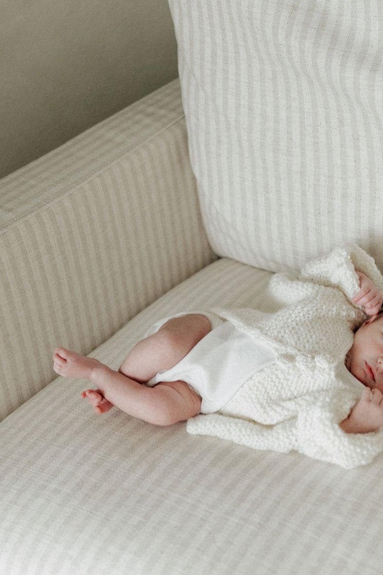 A baby wearing a knitted sweater and diaper lying on a striped couch.