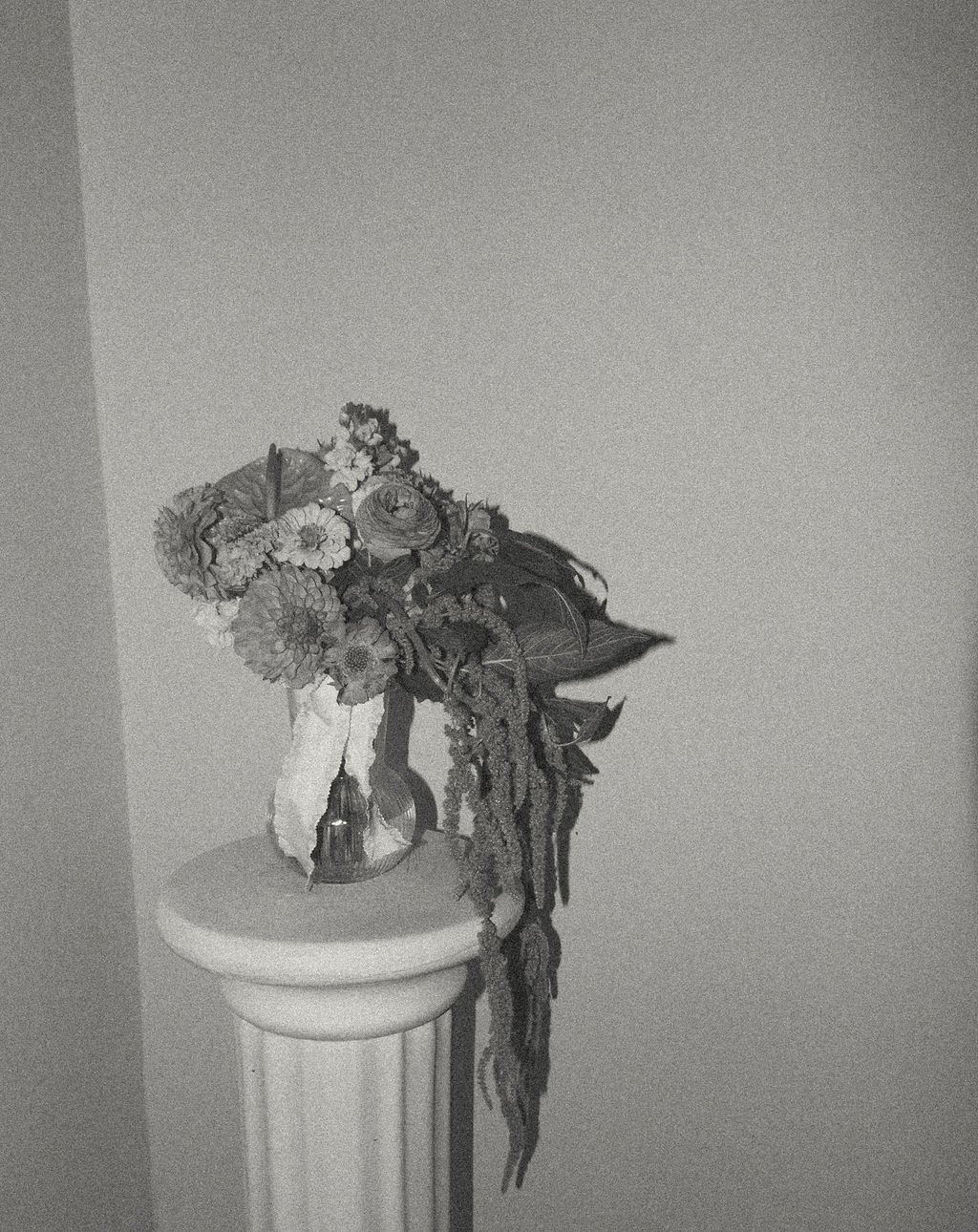 Black and white photo of a vase with flowers on a pedestal.