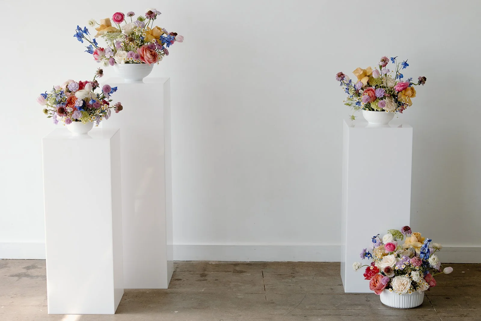 Floral arrangements on white pedestals in a minimalist setting.