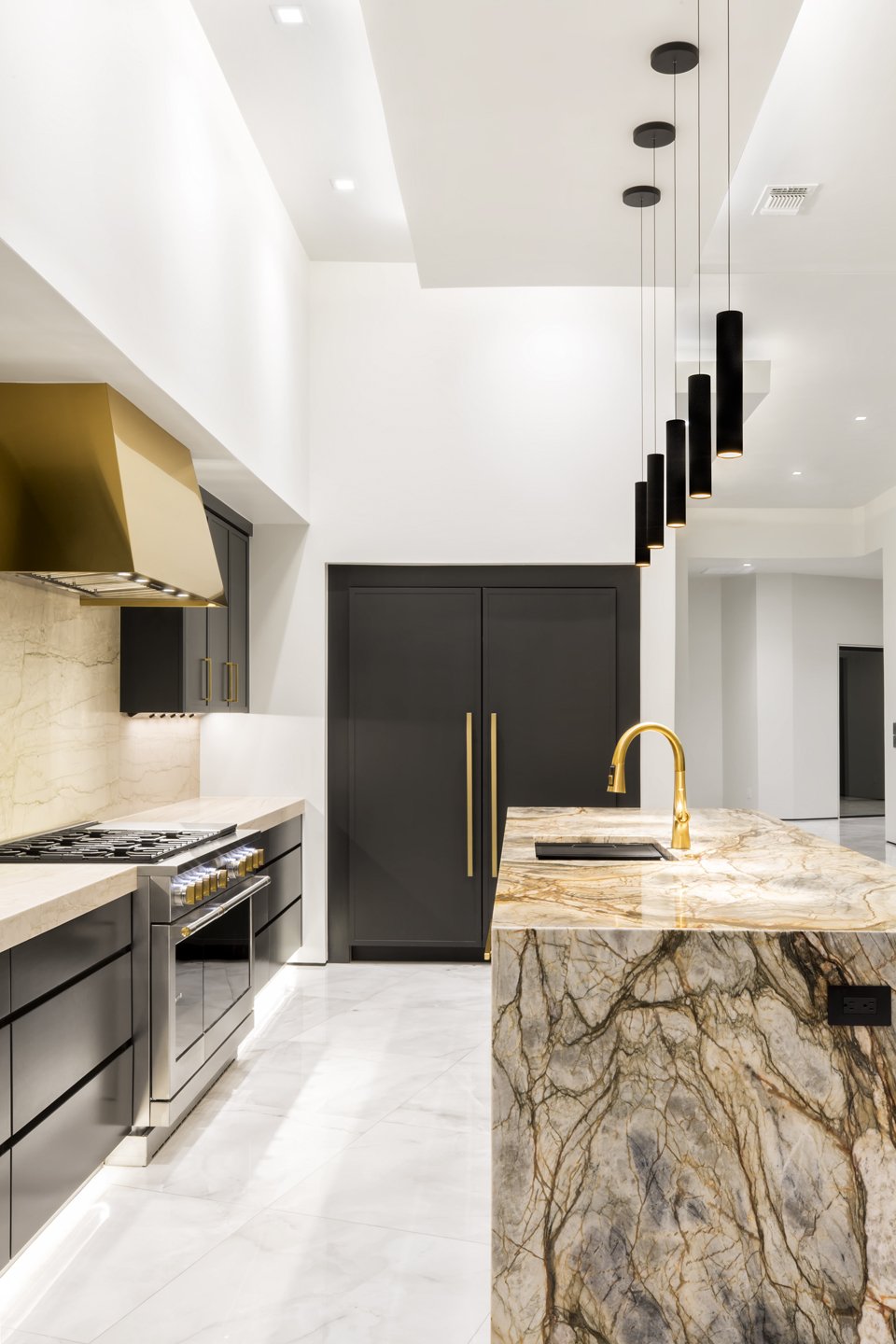 Modern kitchen with black cabinets, gold handles, marble countertops, a built-in stove, and overhanging pendant lights.