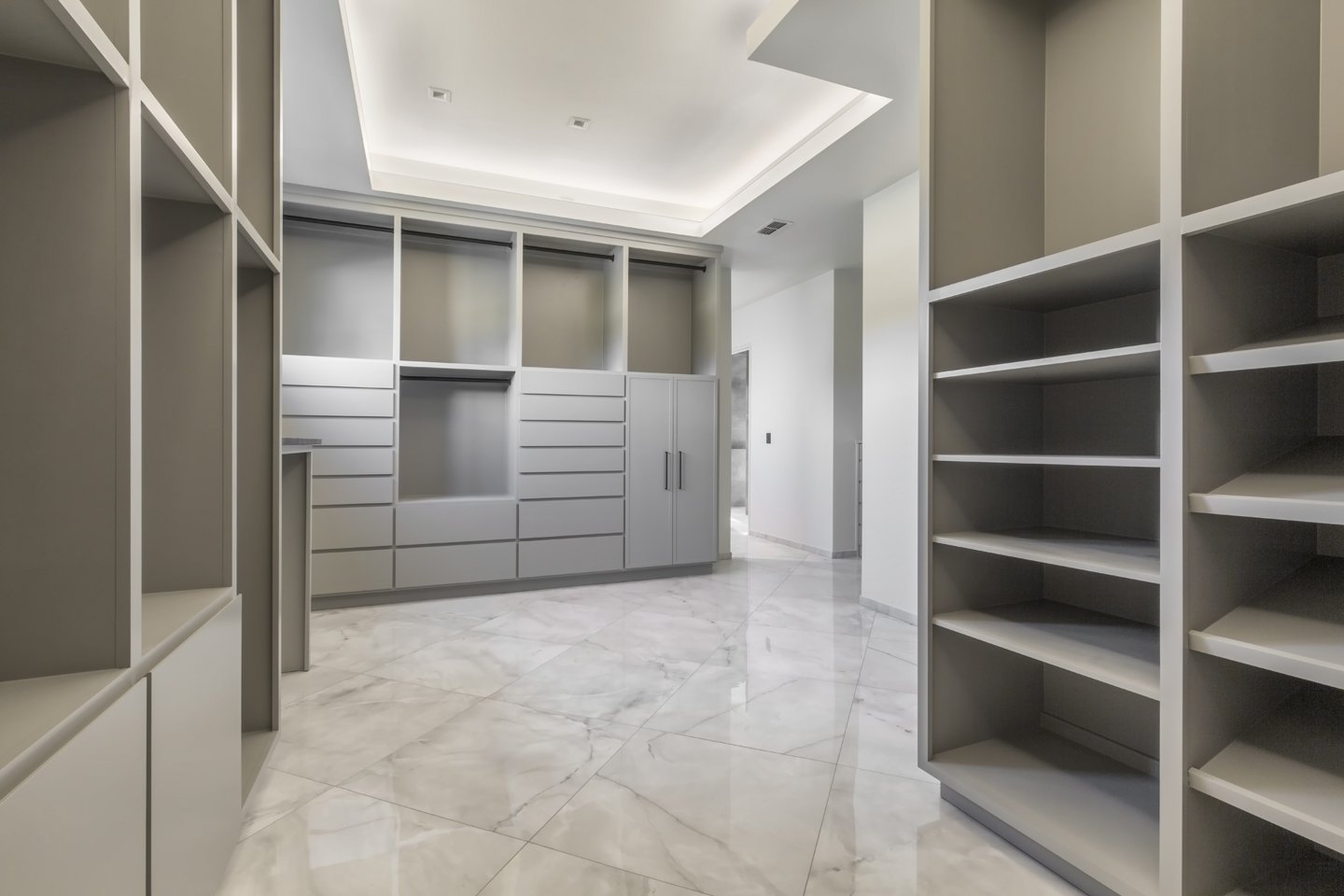 Empty walk-in closet with built-in shelves and lockers, marble floor, and bright ceiling lighting.