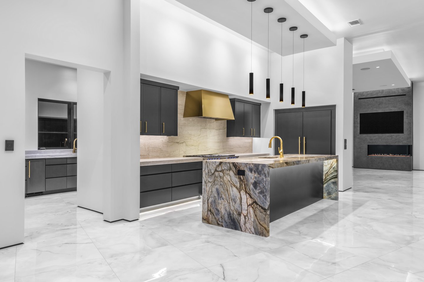 Modern kitchen with black cabinets, gold accents, marble countertops, and a marble island with a gold faucet.