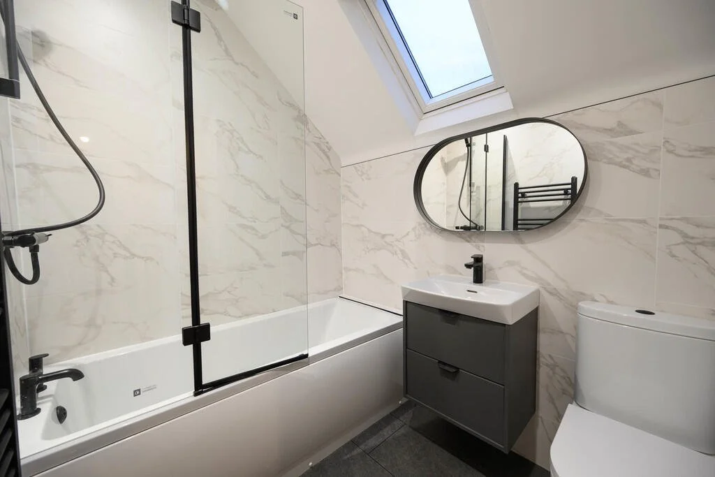 Merritt Estates. Modern bathroom with a bathtub, shower, vanity sink, oval mirror, toilet, and skylight.