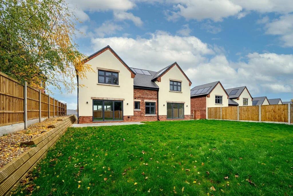 Merritt Estates. Newly built modern houses with brick and cream siding in a suburban neighbourhood, surrounded by a green lawn, wooden fences, and a partly cloudy sky.