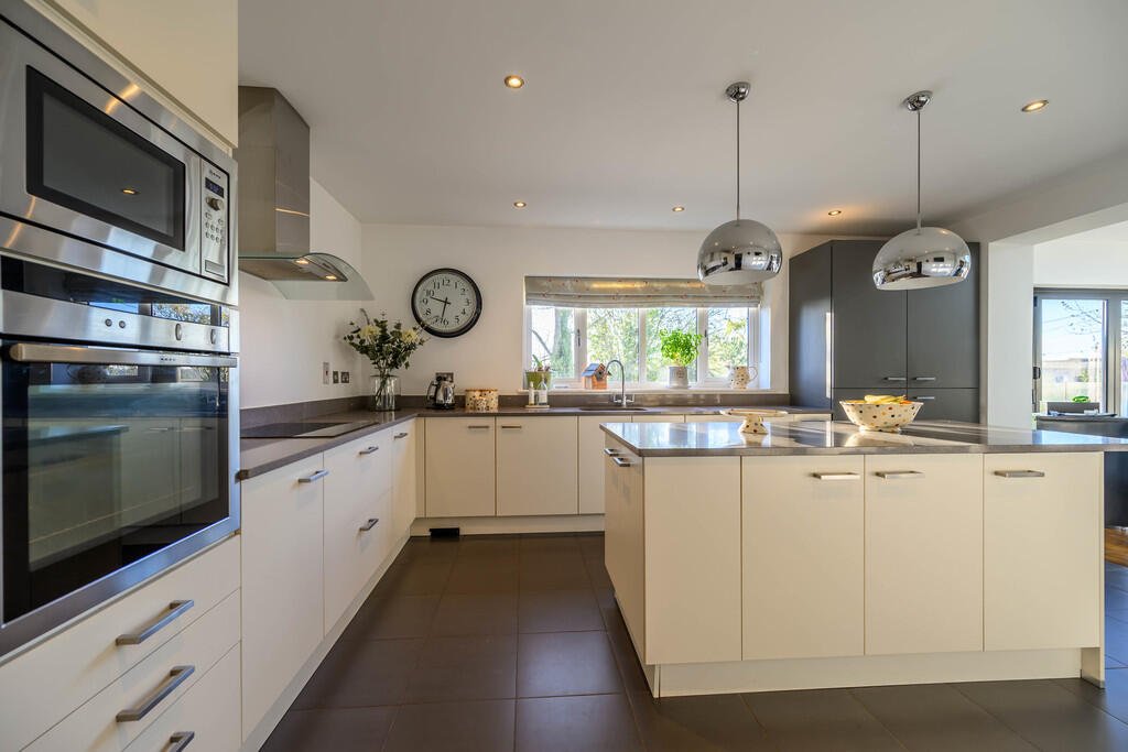 Modern kitchen with white cabinets, stainless steel appliances, gray countertops, a window with plant, and two hanging metallic pendant lights.