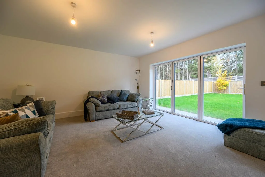 Merritt Estates. Living room with sofas, a glass coffee table, and large sliding glass doors leading to a backyard with green grass and a wooden fence.