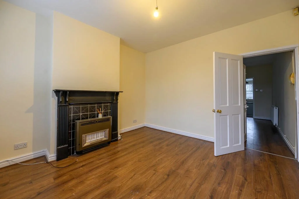 Merritt Estates. Empty room with light yellow walls, wooden floor, a decorative black fireplace with a black and gold heater, a white door open to a hallway, and a ceiling light