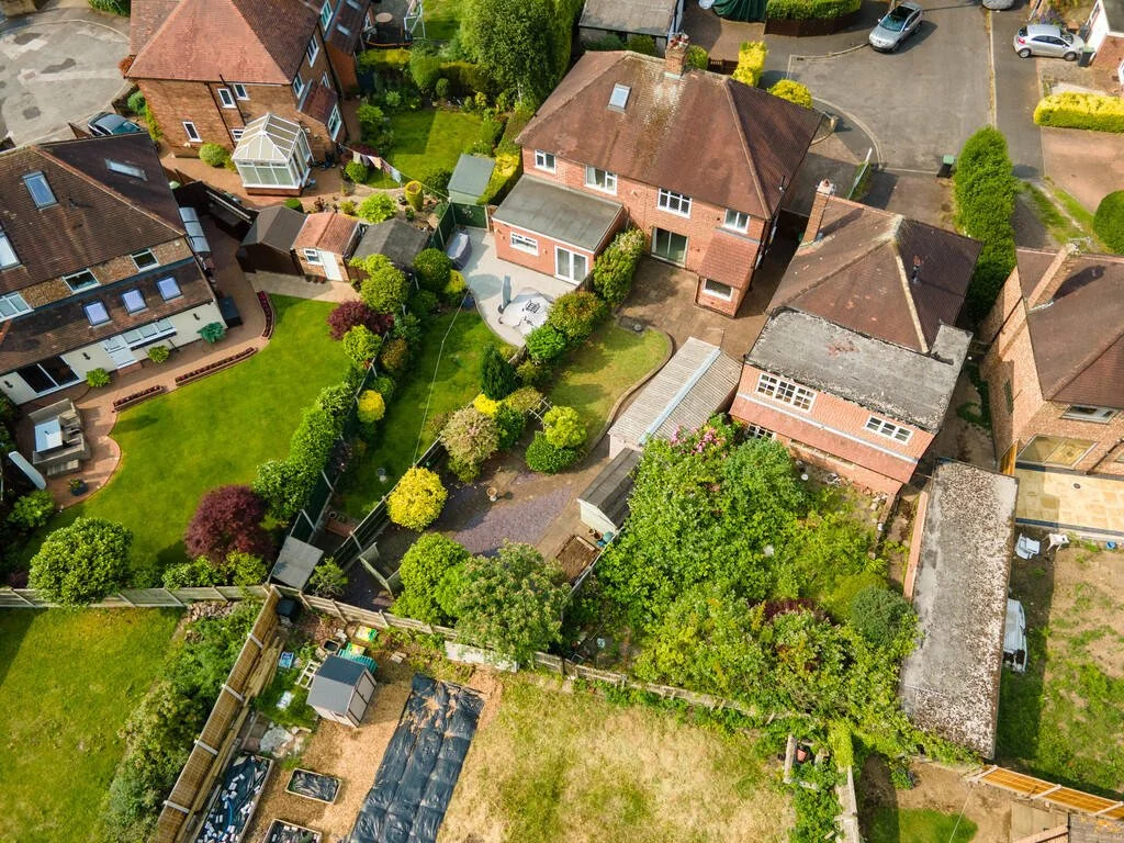 Merritt Estates. Aerial view of a suburban area showing multiple houses with backyards, gardens, and greenery. The houses have various roof styles and colours, with some featuring patios, sheds, and greenhouses.