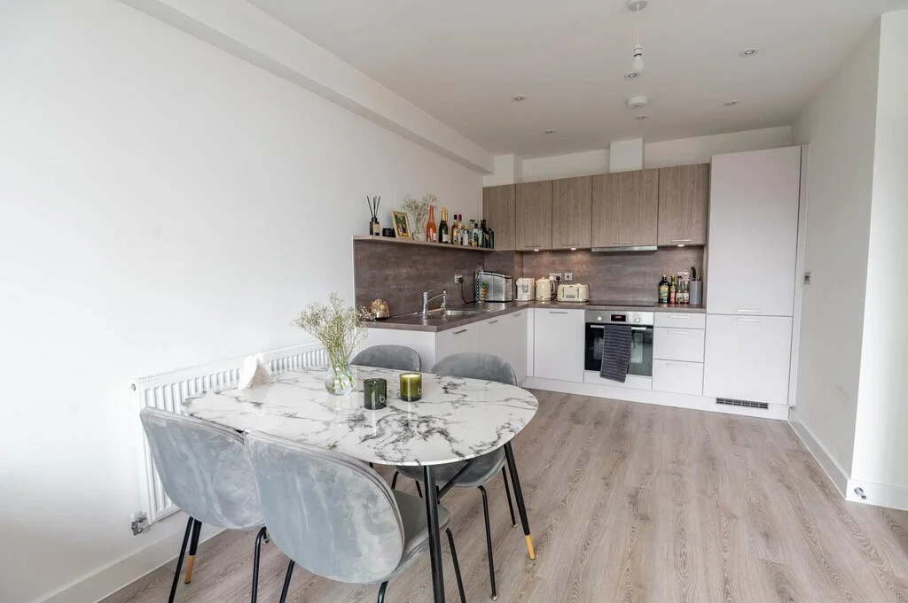 Modern kitchen with a marble dining table and four gray velvet chairs, light wood cabinetry, and a minimalist decor.