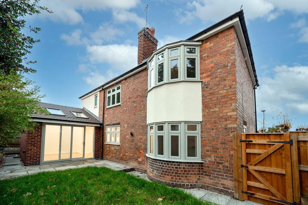 Merritt Estates. Backyard of a brick house with a lawn and a wooden gate, showing a house with a bay window and a conservatory with a glass door.