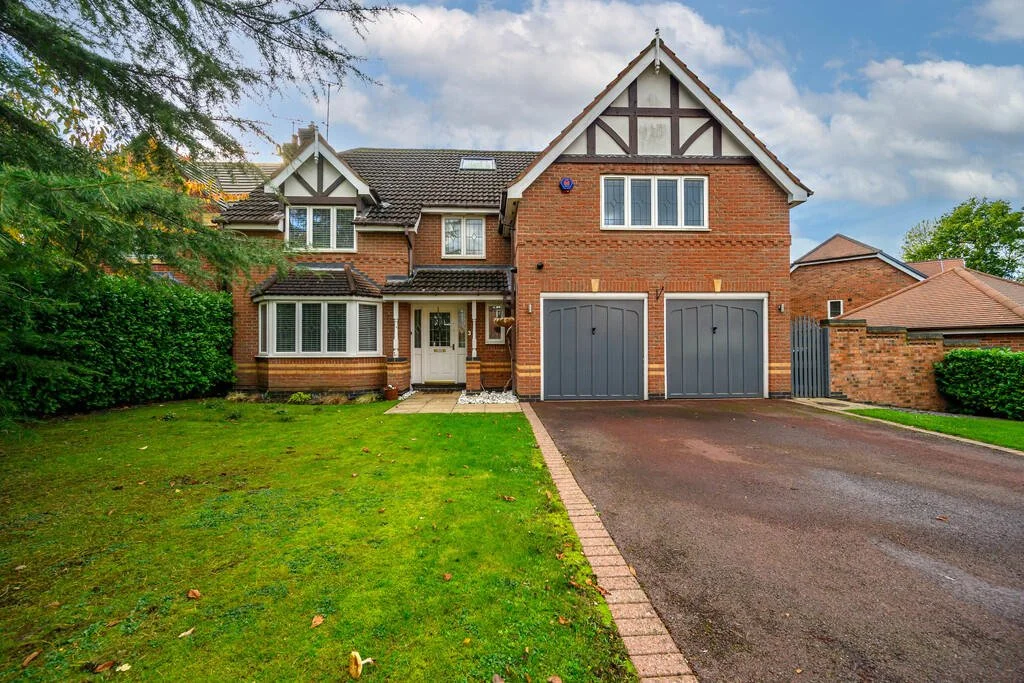 Merritt Estates. A two-story brick house with a front lawn, driveway, and two garage doors. The house features white window frames and a gabled roof with decorative bargeboards.