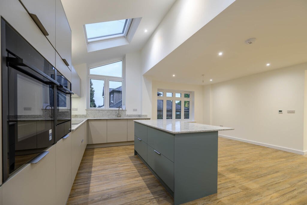 Merritt Estates. Modern kitchen with beige cabinets, a blue kitchen island, marble countertops, wooden flooring, large windows, and skylights.