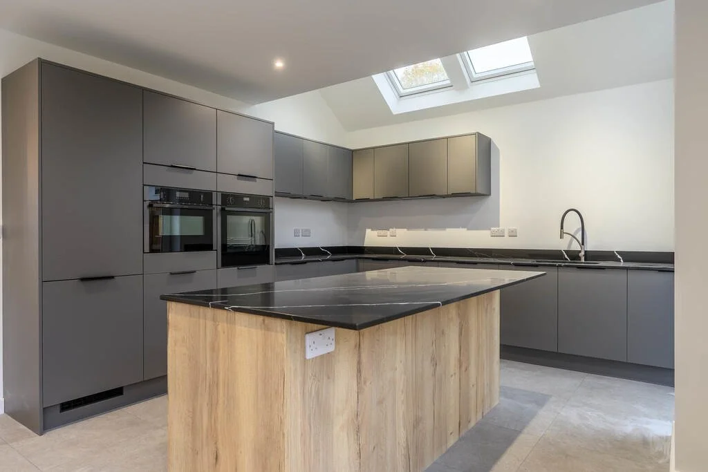 Merritt Estates. Modern kitchen with grey cabinets, black countertops, a wooden island, skylights, and built-in oven and microwave.