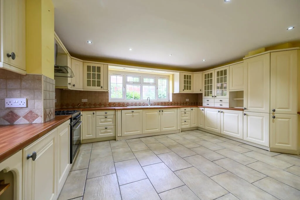 Empty kitchen with cream cabinets, brown countertops, tiled backsplash, and large window.
