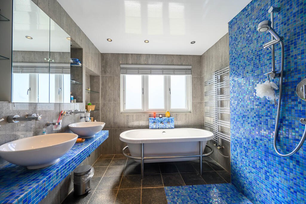 Modern bathroom with double sink, bathtub, and walk-in shower with blue mosaic tiles.